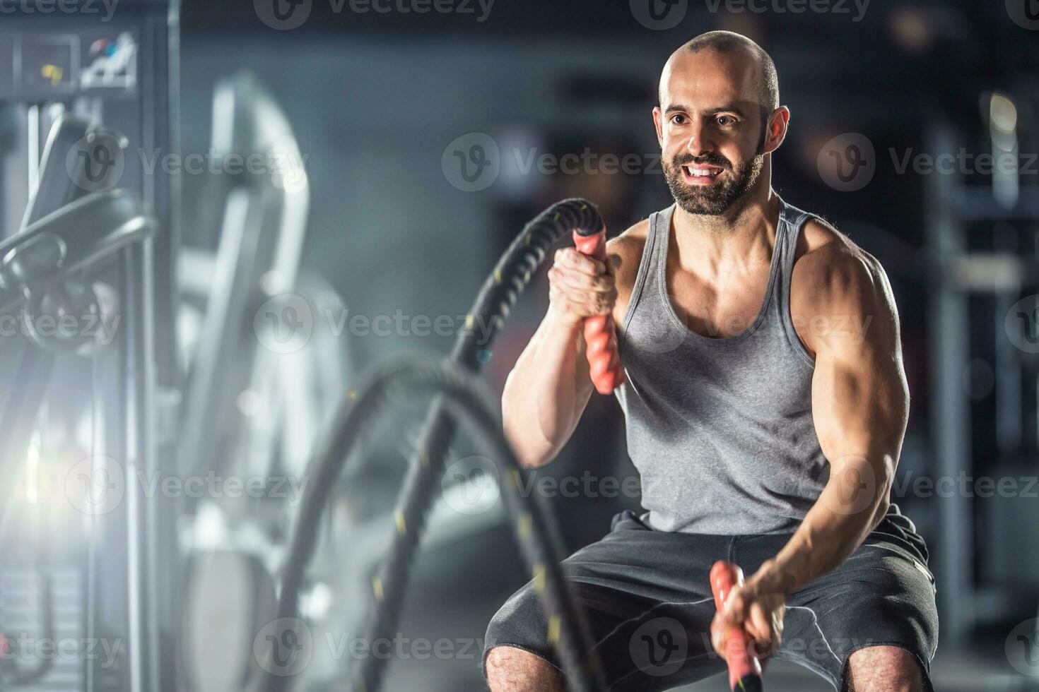 Muscular man exercising with battle ropes at the fitness gym photo