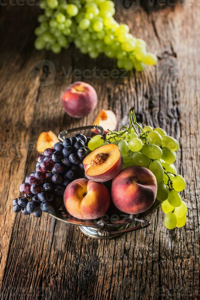 Ripe grapes and peaches in rustic bowl and wooden table photo