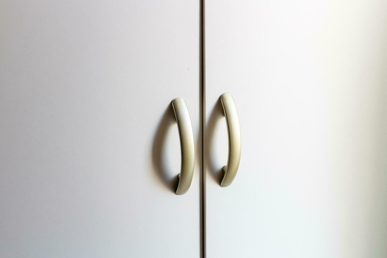 Close up of a white cupboard door with two white handles. photo