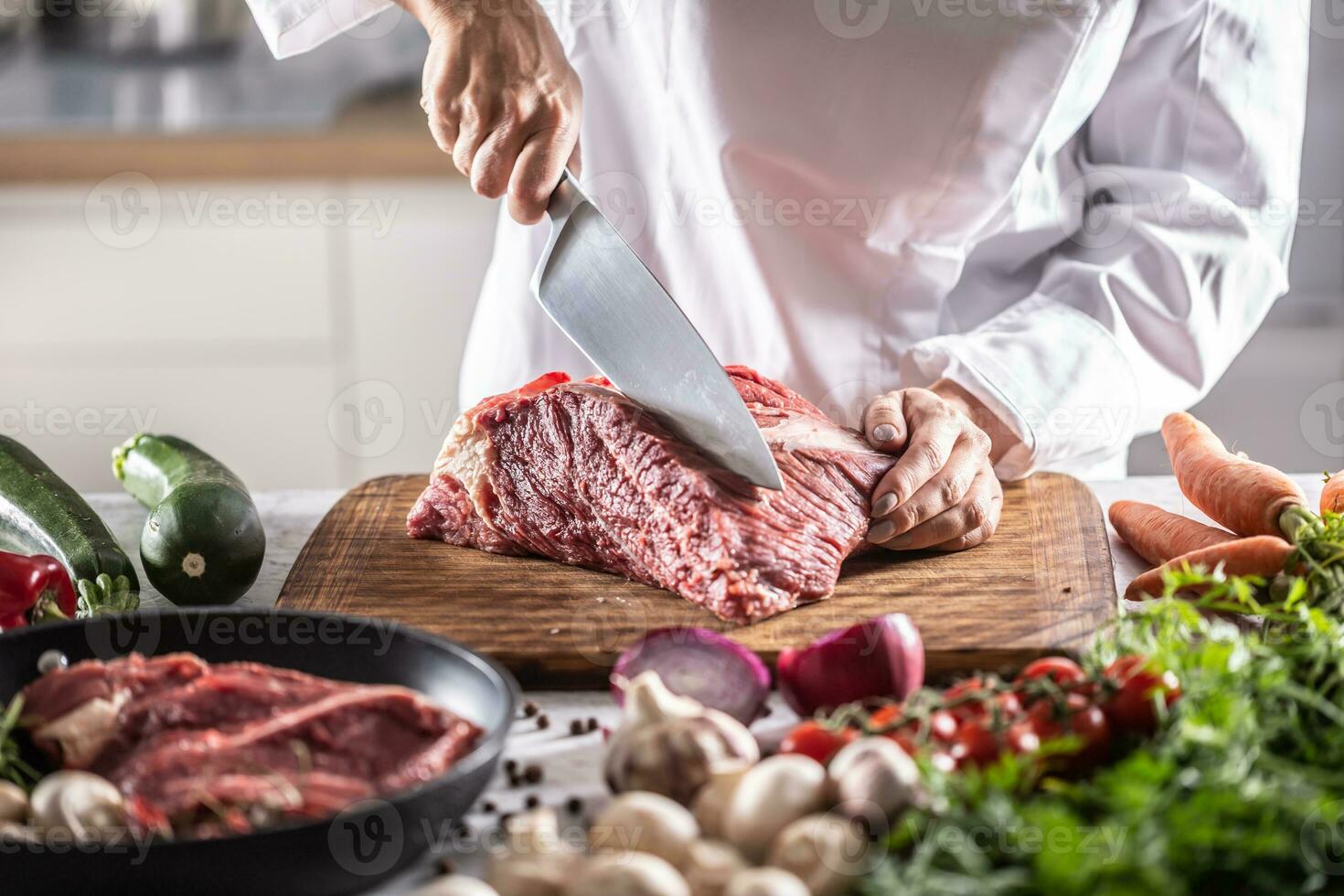 Chef cuts a slice from a chunk of red meat by a big knife in the restaurant photo