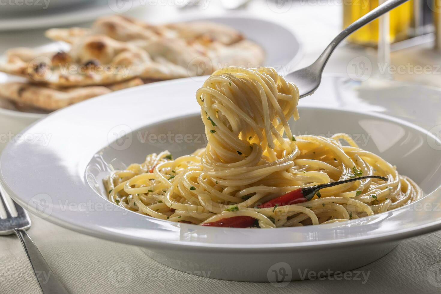 Spaghetti aglio e olio spinned on a fork taking a mouthful portion of pasta out of the plate photo