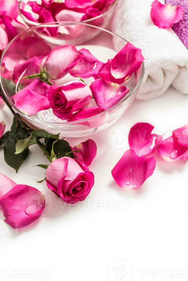 Pink roses petals in bowl with towels and pure water over white.. Spa and wellness concept photo