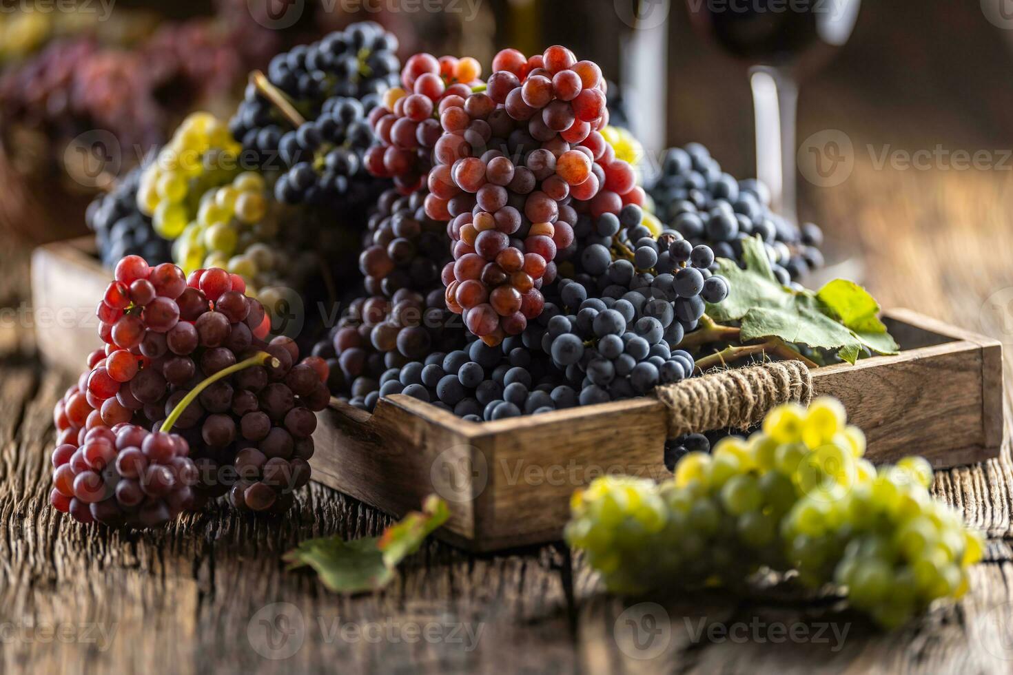 Juicy bunches of grapes in a wooden box, red wine in the background photo