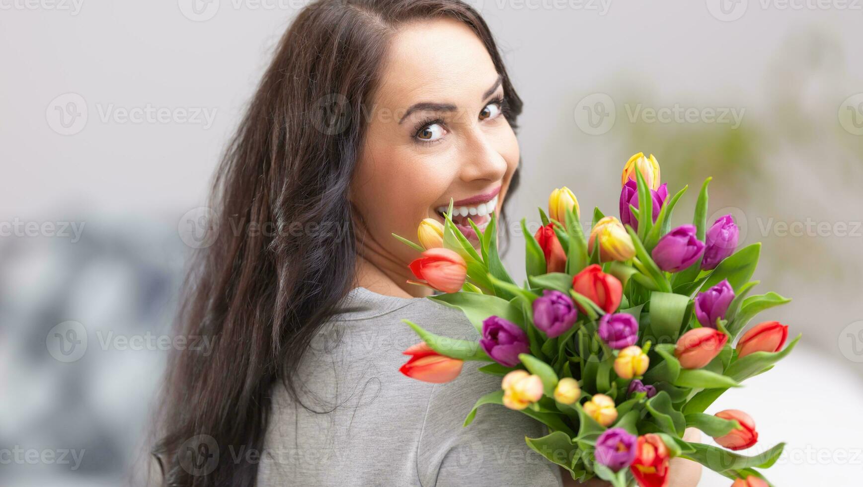 Happy dark haired woman holding a lovely bouquet full of tulips during national womens day photo