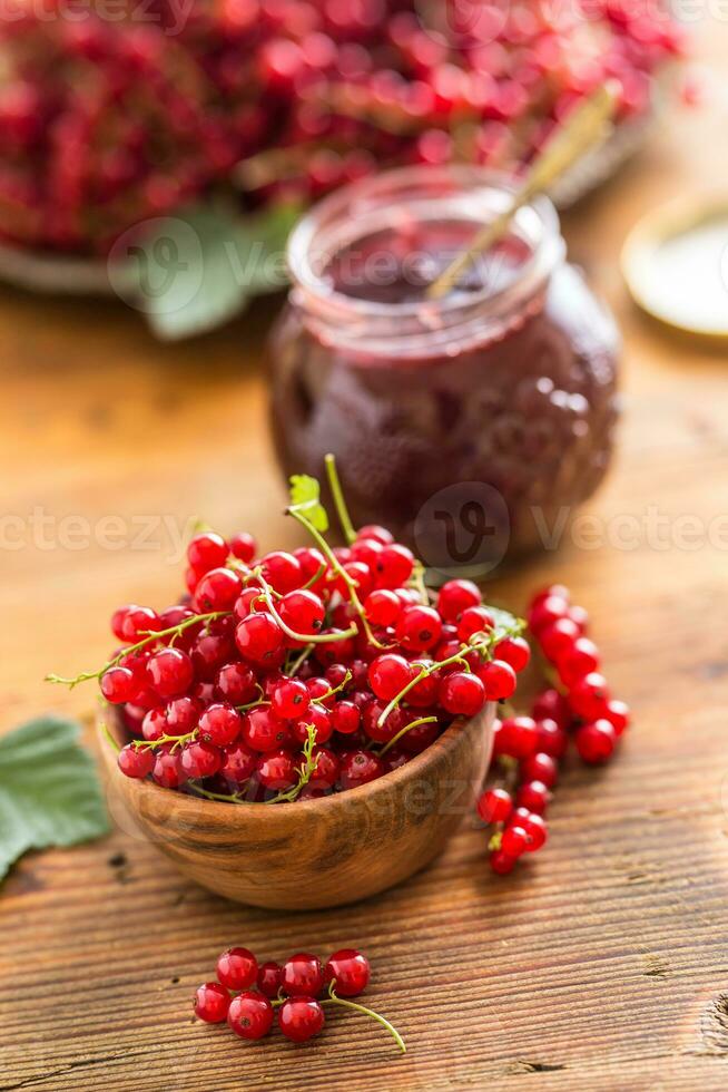 Fresh red currants in bowl and jam marmalade on wooden table photo
