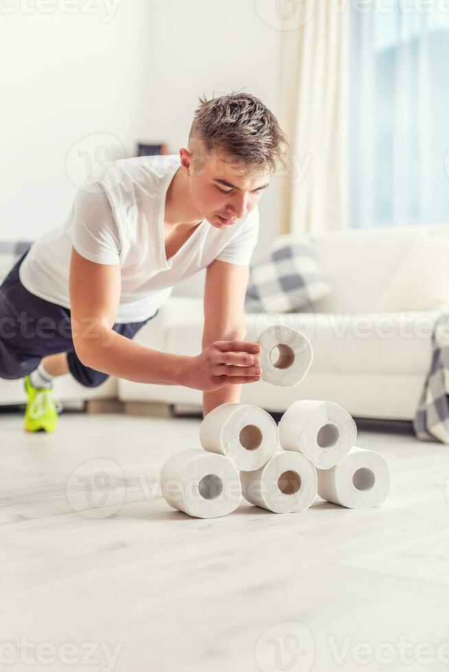 Fit young man creatively using excess toilet paper rolls for home plank and pushups workout in the living room. photo