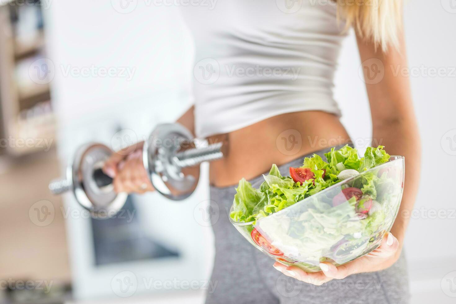 Woman holding bowl from fresh vegetable salad and dumbbell. photo