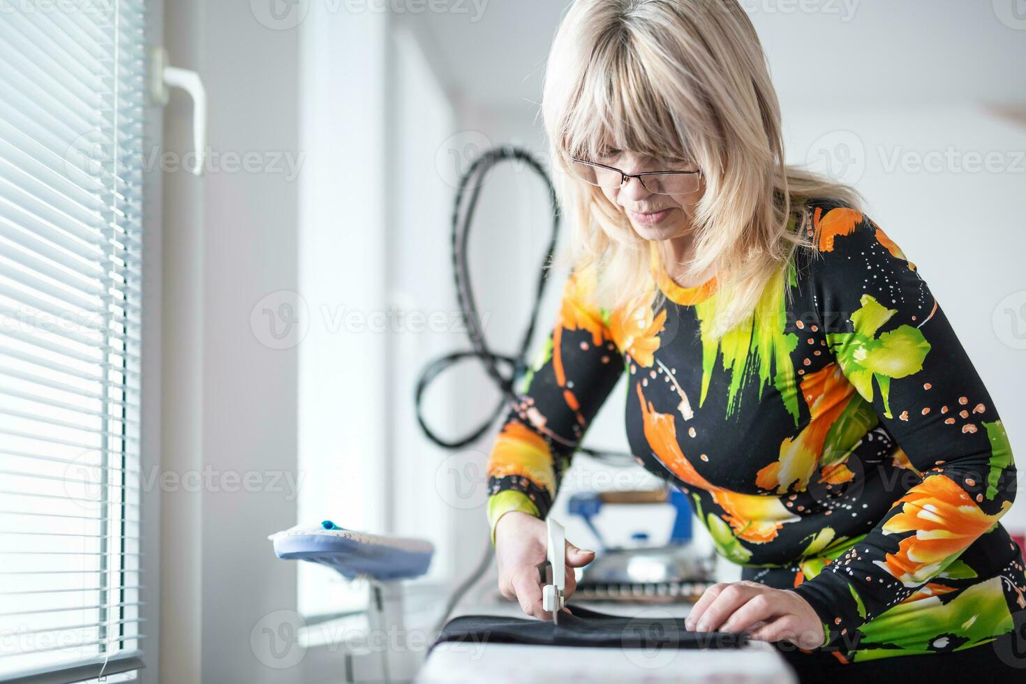 Female tailor cuts fabric with scissors in her own workshop photo