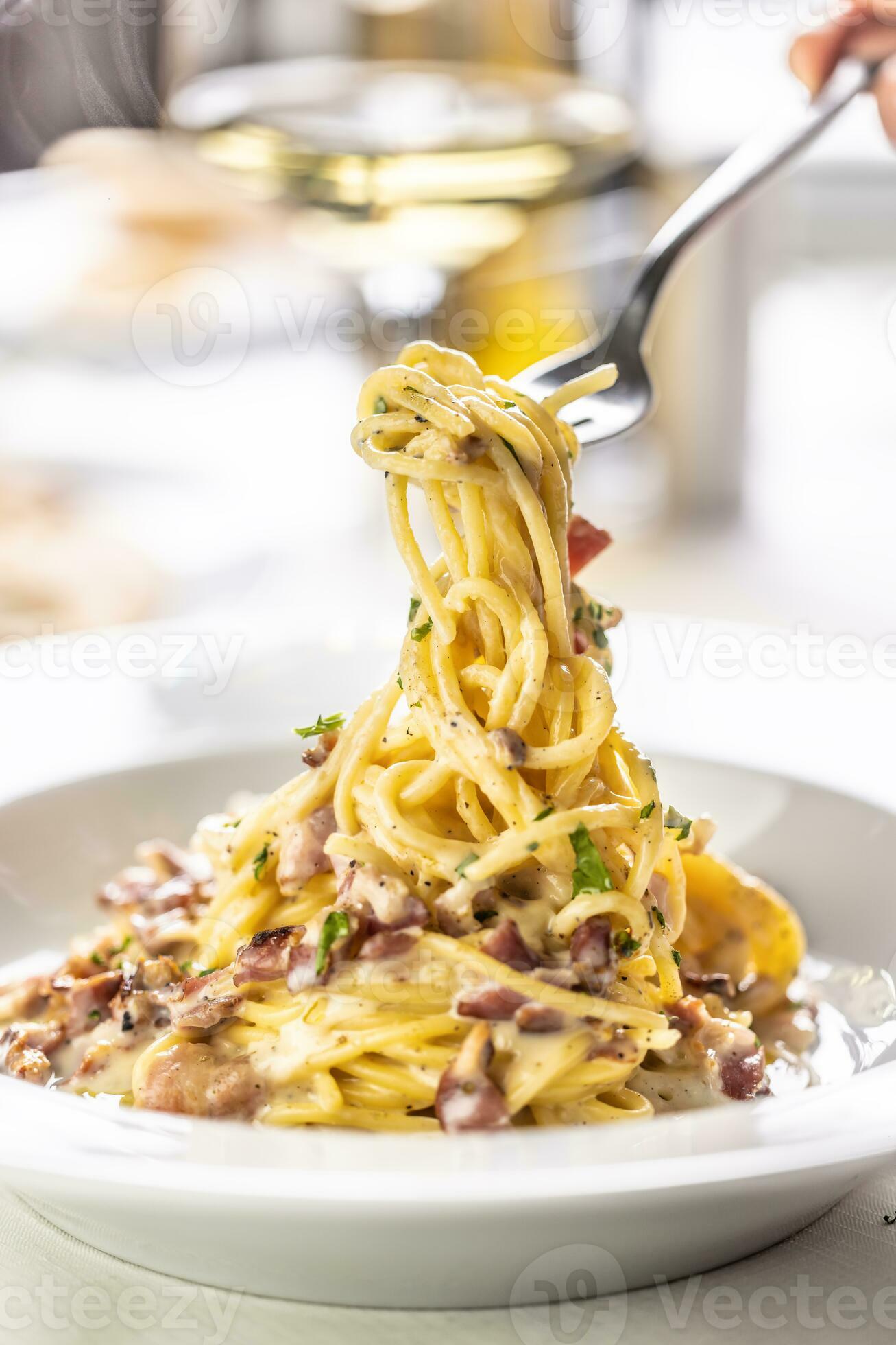 Detail of a fork spinning spaghetti carbonara from a full plate