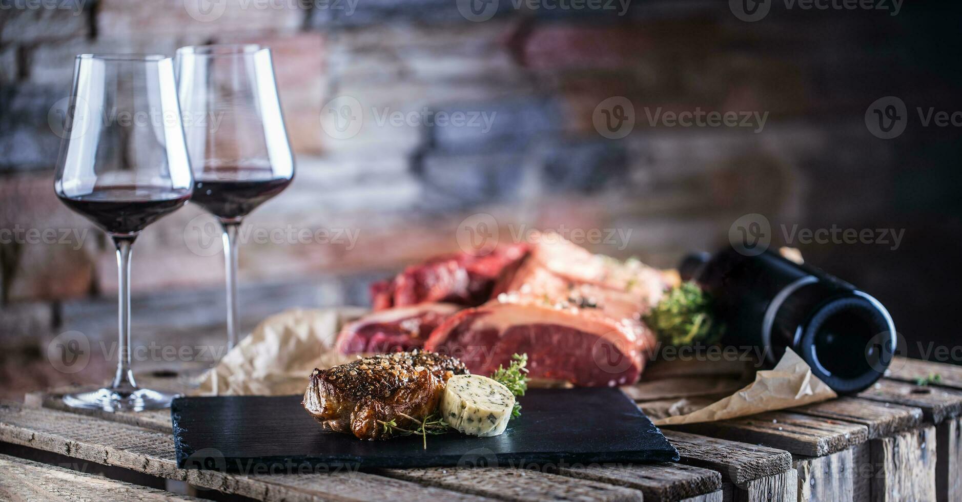 Two cups with red wine roasted and raw beef steak on slate board photo