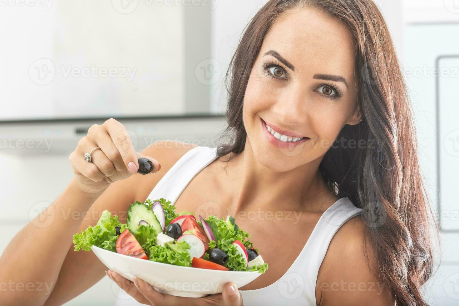 Brunette good-looking woman eating healthy colorful fitness salad with olive in her hand photo