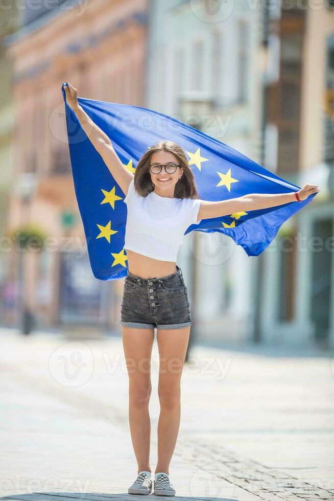 Cute happy young girl with the flag of the European Union in the streets somewhere in europe photo