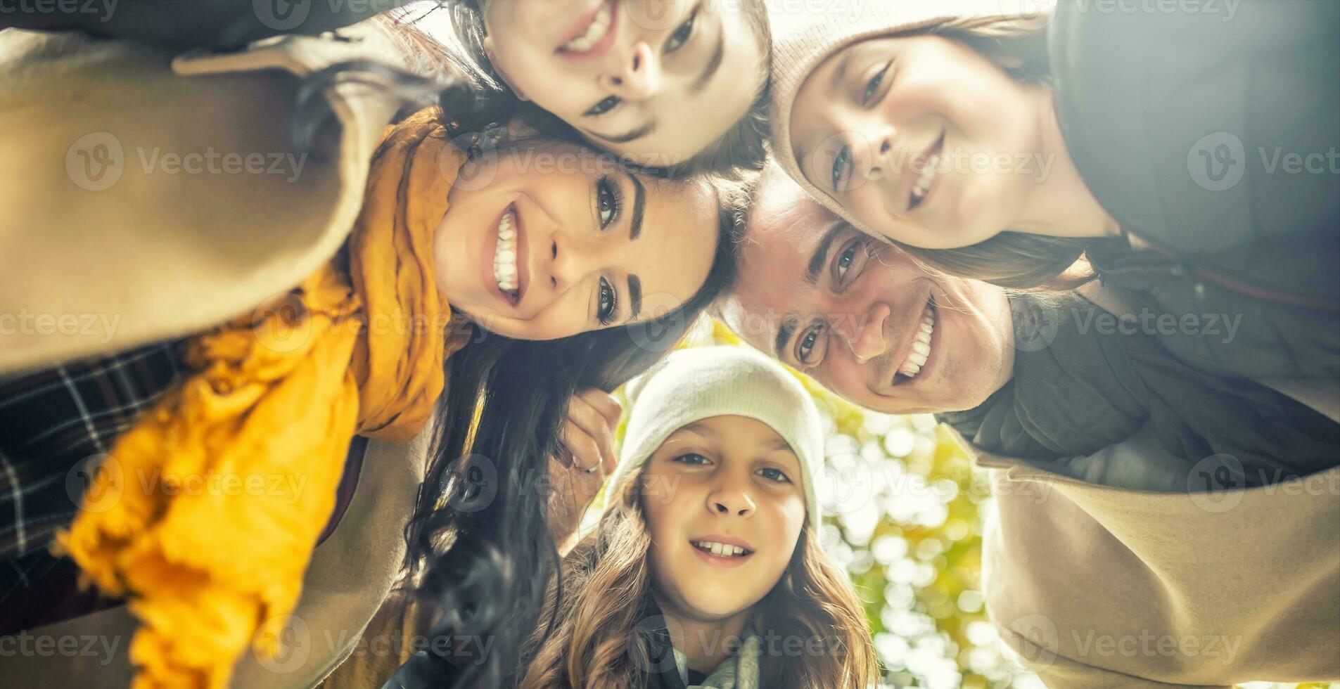 Photo from below on a happy family with three kids smiling, putting their heads together