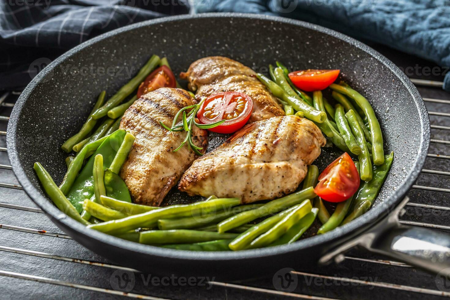 sano receta de A la parrilla pollo, verde vegetal y Tomates en un oscuro antiadherente pan metido en metalico cuadrícula y oscuro antecedentes foto