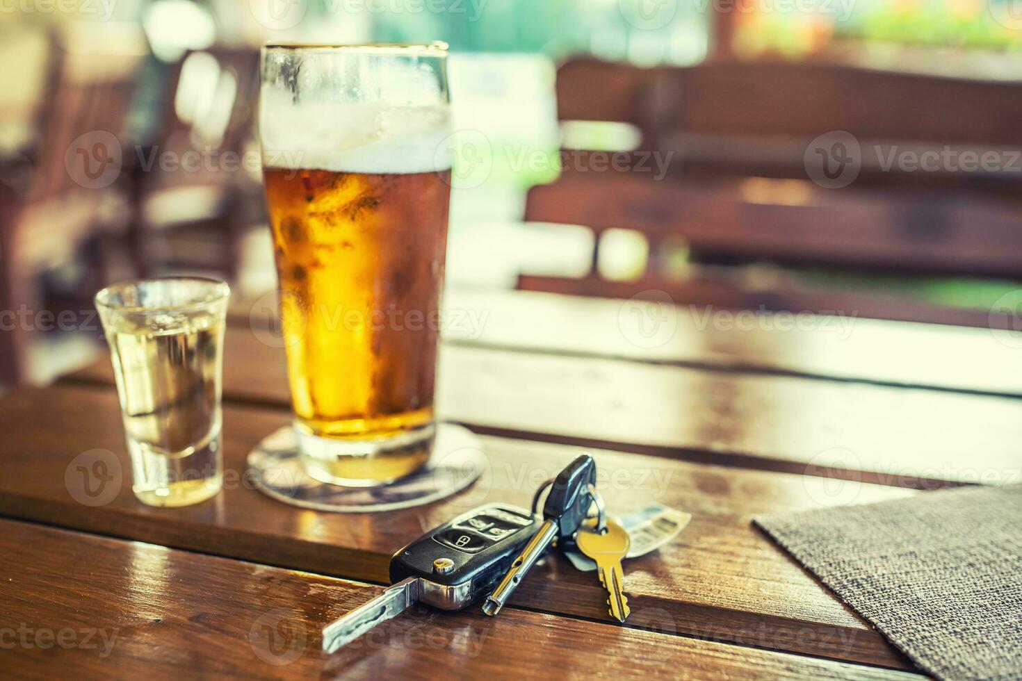 Car keys and glass of beer or distillate alcohol on table in pub or restaurant photo