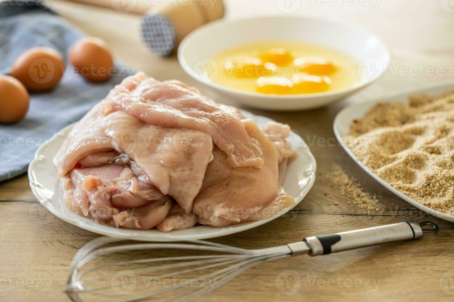 Raw chicken breasts, bread crumbs and eggs with whisker ready for making schnitzels photo
