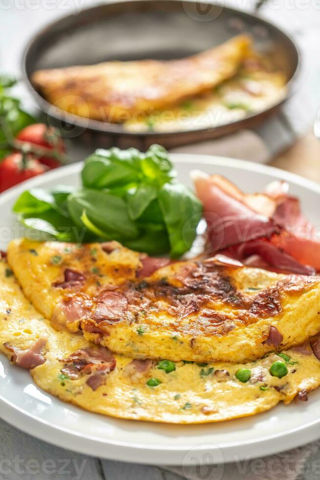 Omelette with prosciutto peas basil tomatoes and herbs on white plate photo