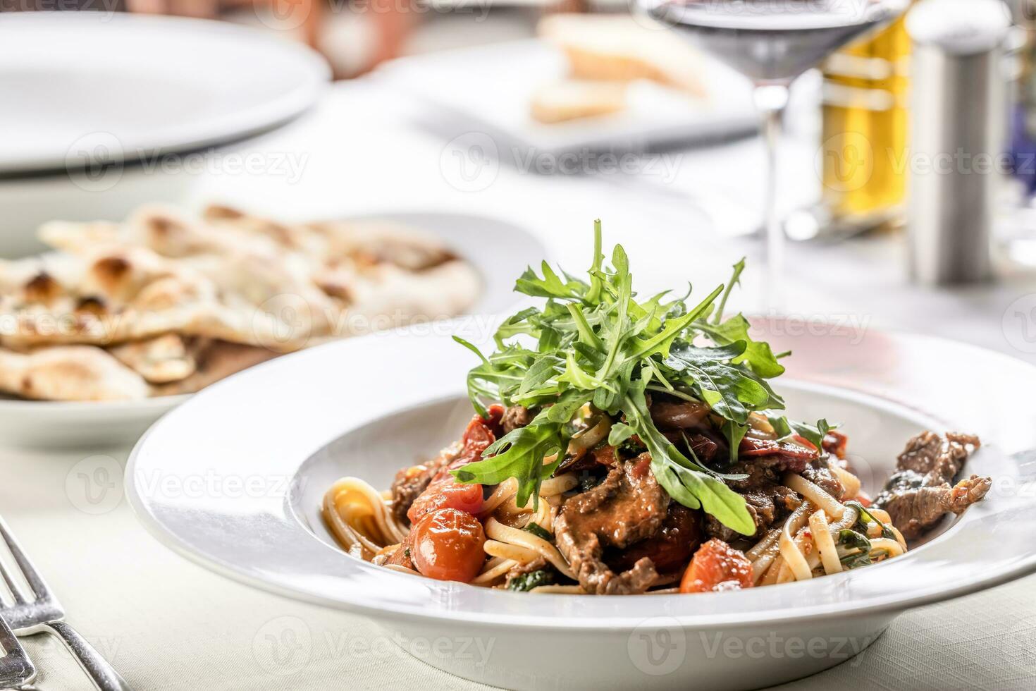 Linguine with tomatoes and tender beef meat served in a plate and topped with rocket salad photo