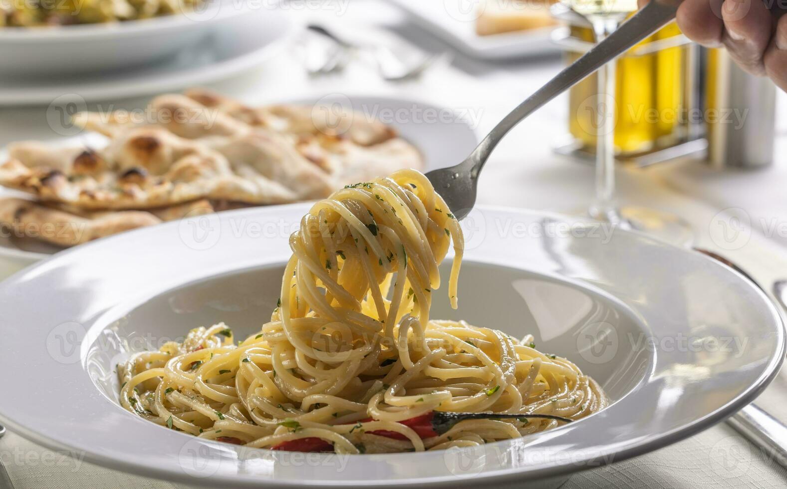 Hand with a fork spinning spaghetti aglio e olio peperoncino from a plate in a restaurant photo