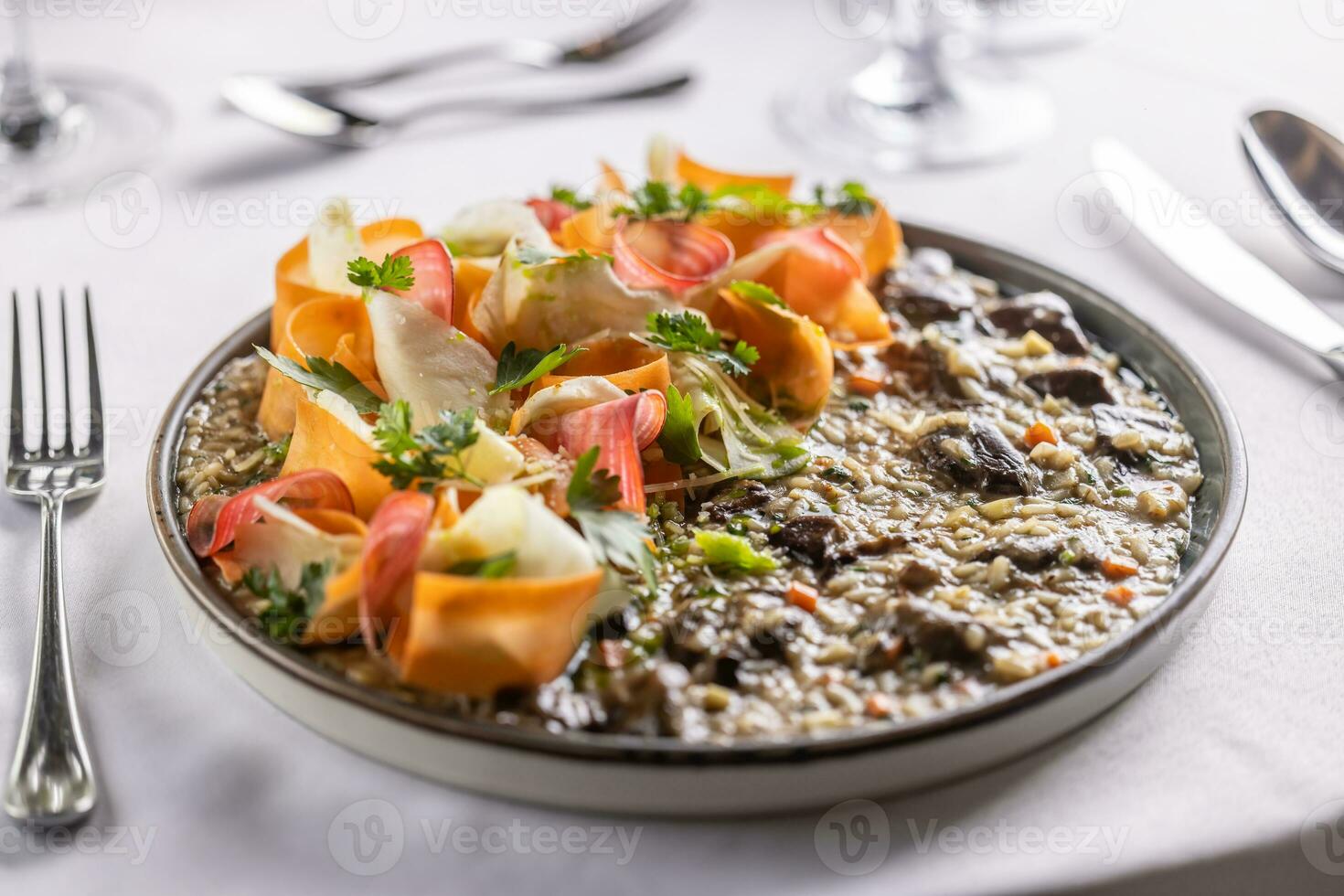 Italian mushroom risotto with root veggies and parsley decoration served in a plate on a restaurant table photo