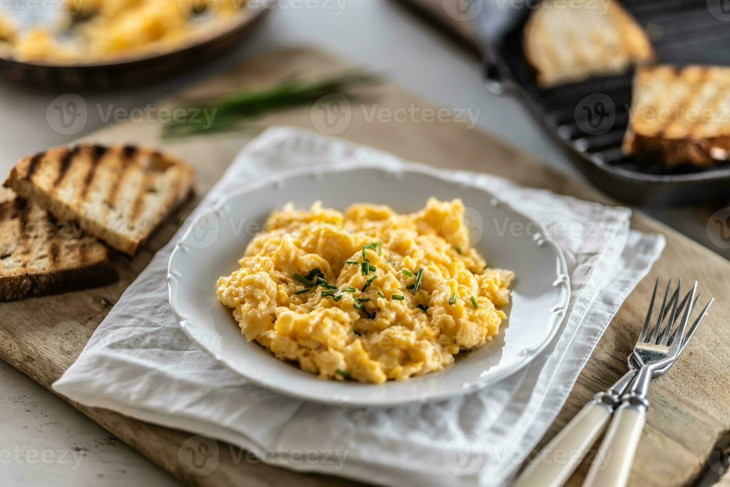 Smooth scrambled eggs and crunchy toasts served in a plate with cutlery on the side photo