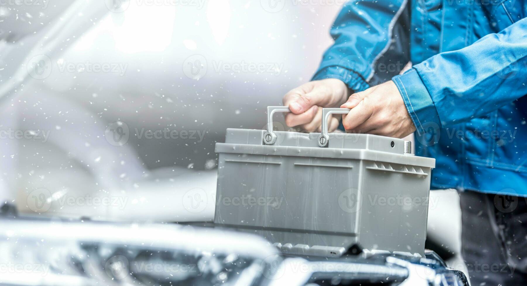 Car technician replaces dead car battery in winter conditions photo