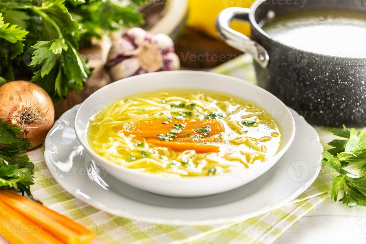 Chicken soup broth in a plate carrot onion celery herbs garlic and fresh vegetables photo