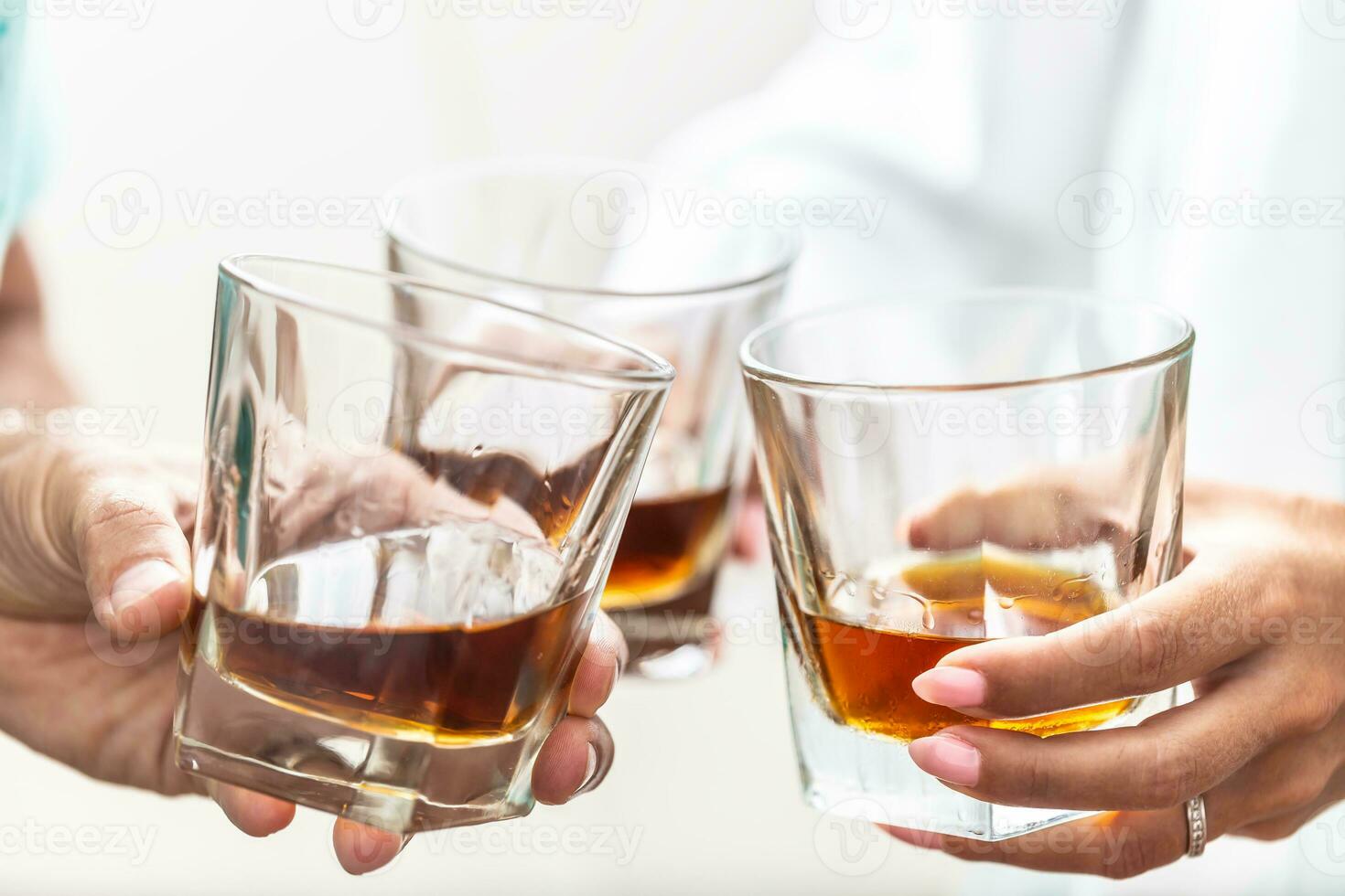 Group of friends toasting with glasses of whiskey brandy or rum indoors - closeup photo