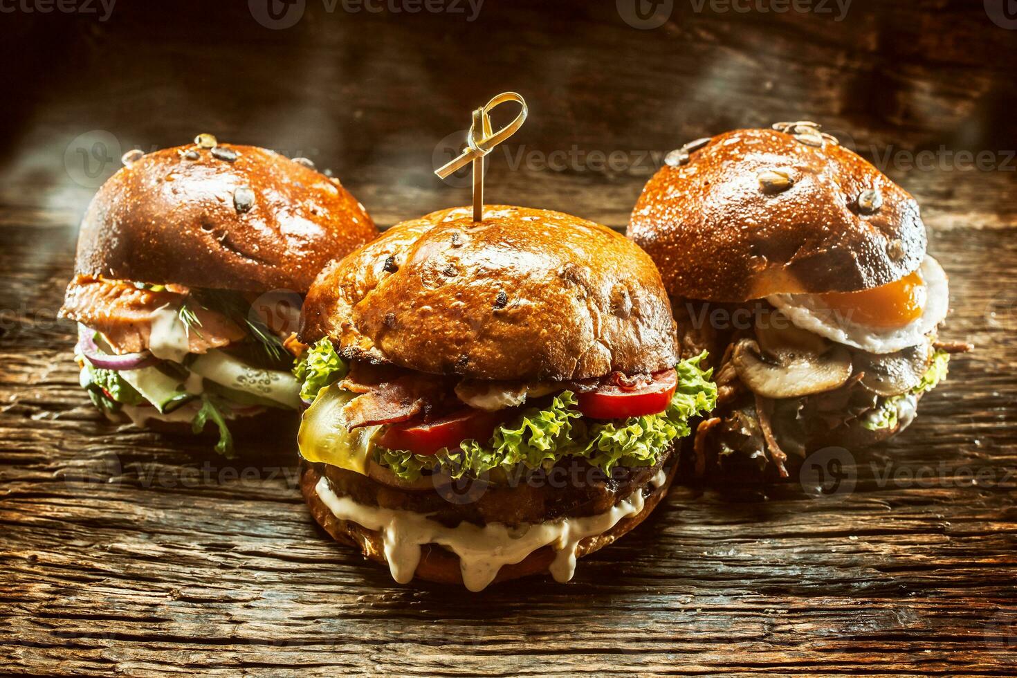 Front view on three large, beef salmon and kebab burgers stuffed with fresh vegetable salad and dressing photo