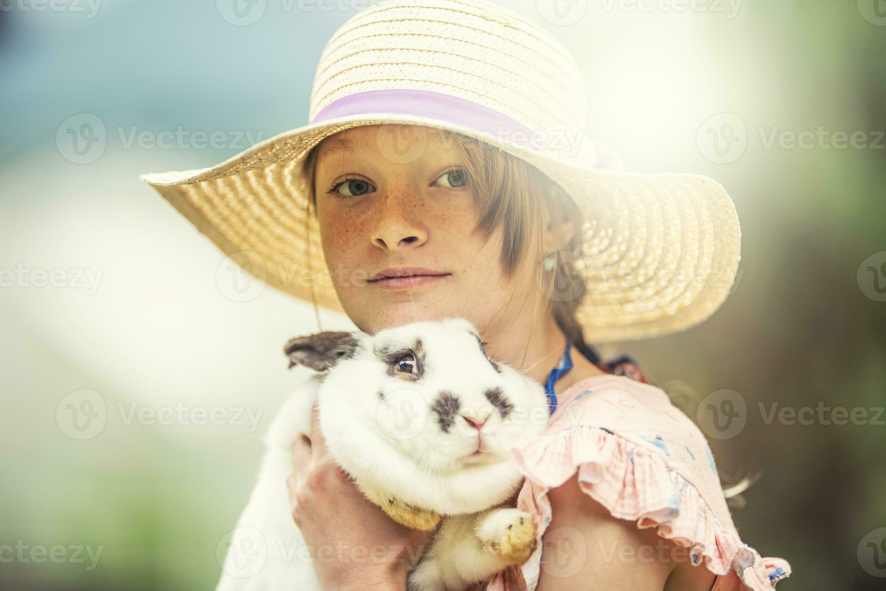 Young kid in a hat holding a scared rabbit in hands. Rabbit is scared