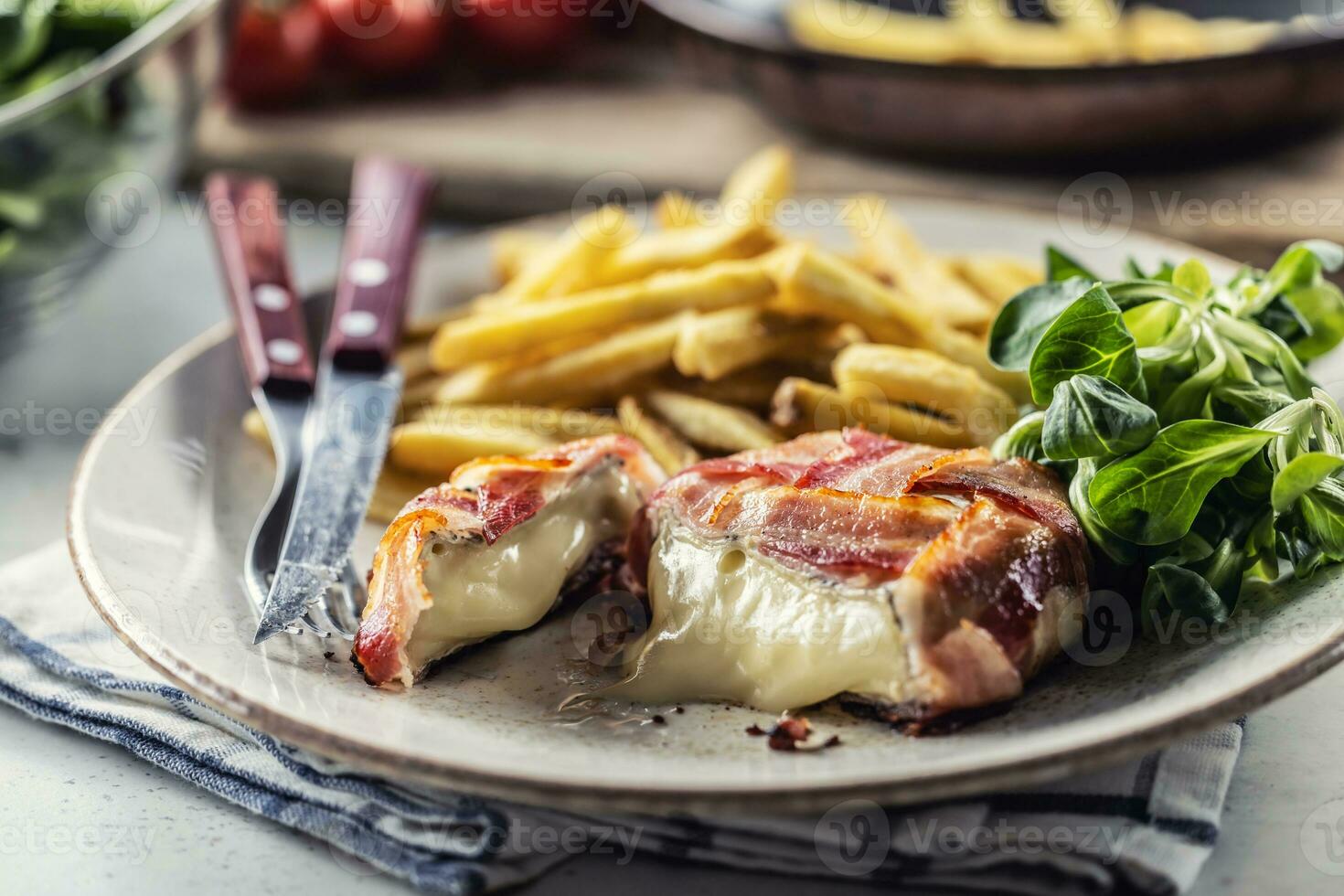Cut melting cheese in a bacon wrap served on a plate with french fries and green salad photo