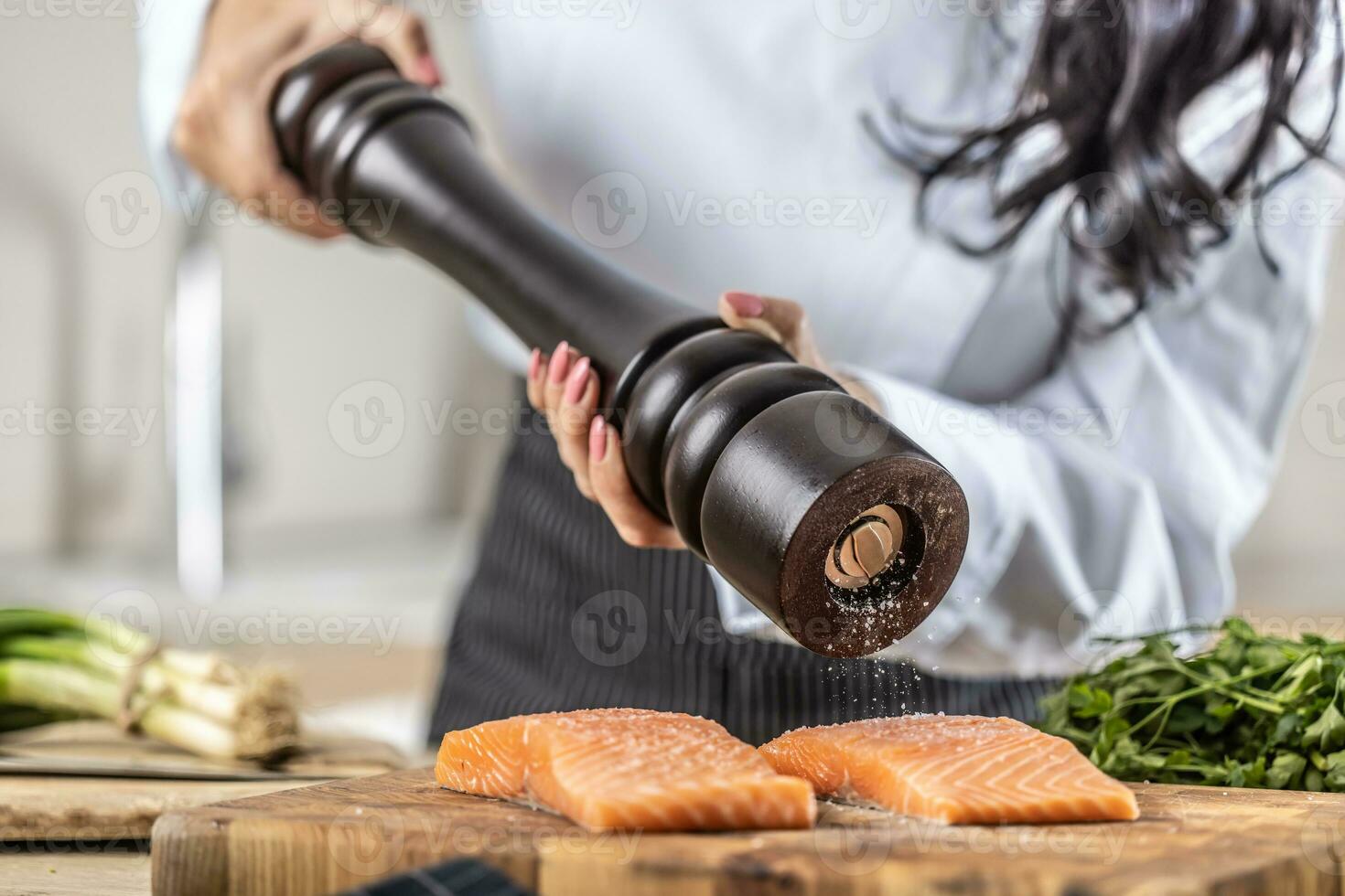 A salt grinder is used by a chef to season salmon in a restaurant kitchen photo