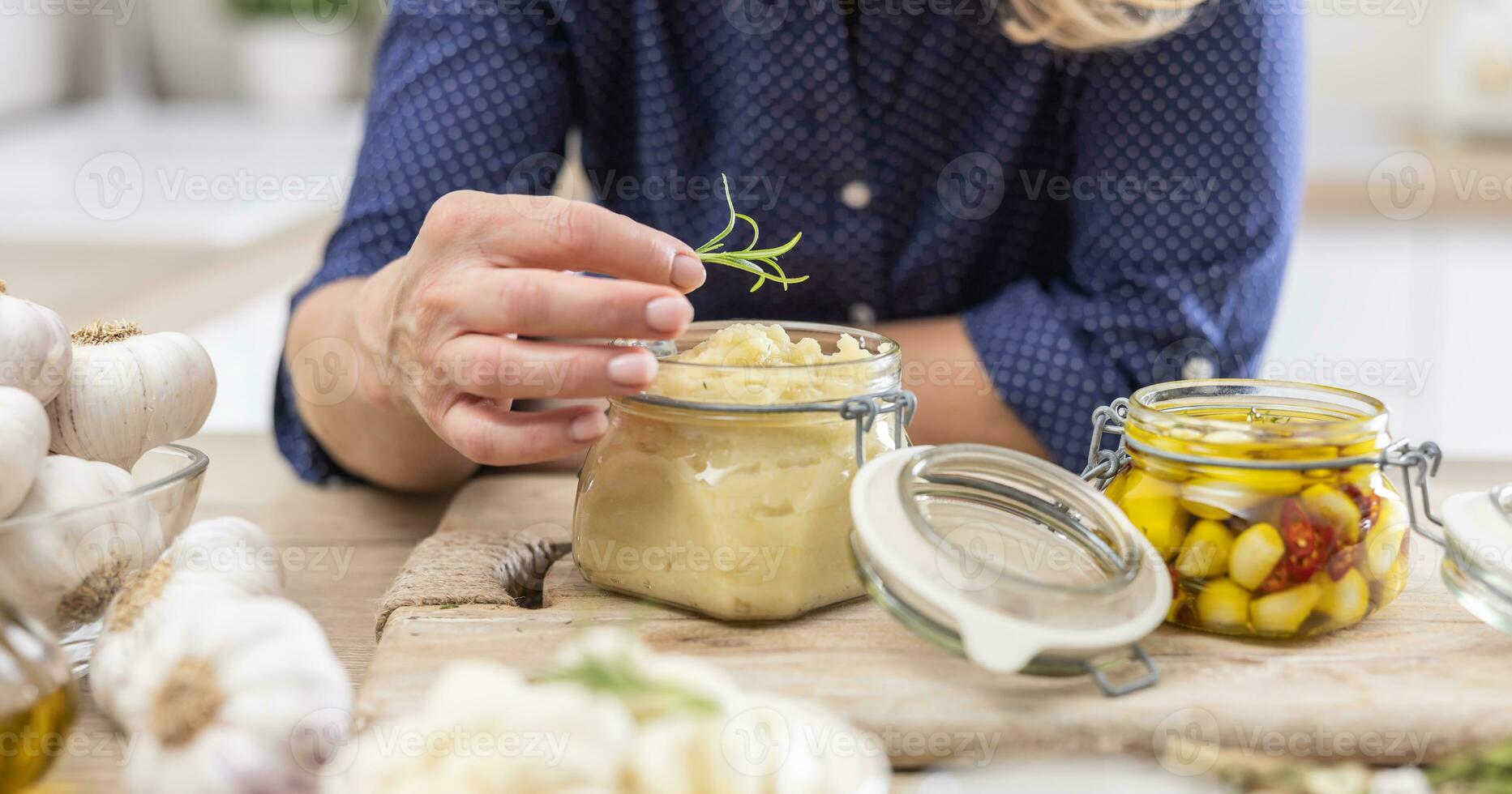 Detail of woman putting a sprig of rosemary on top of a jar full of crushed garlic paste photo