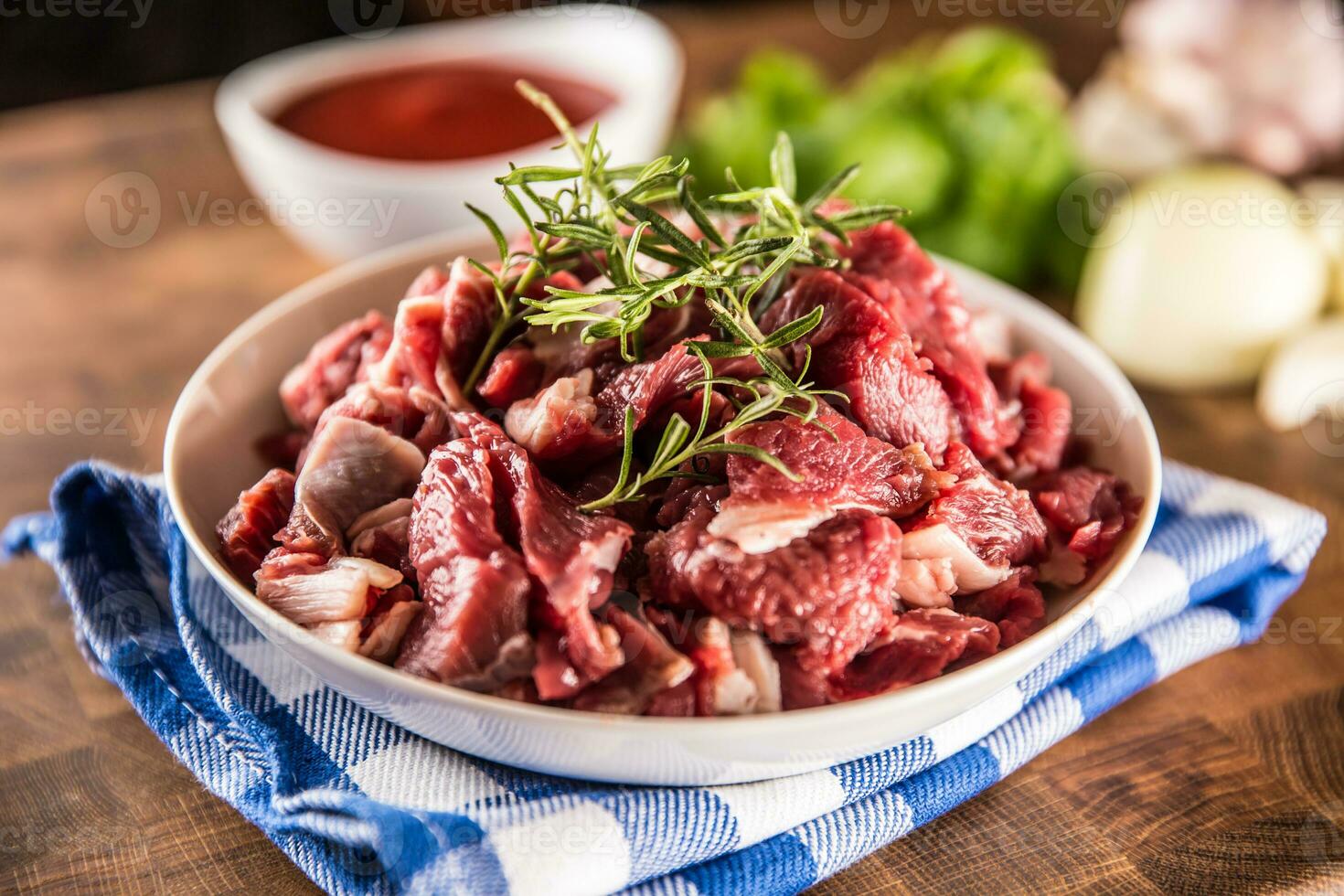 Raw beef pieces with rosemary in bowl on butcher board photo