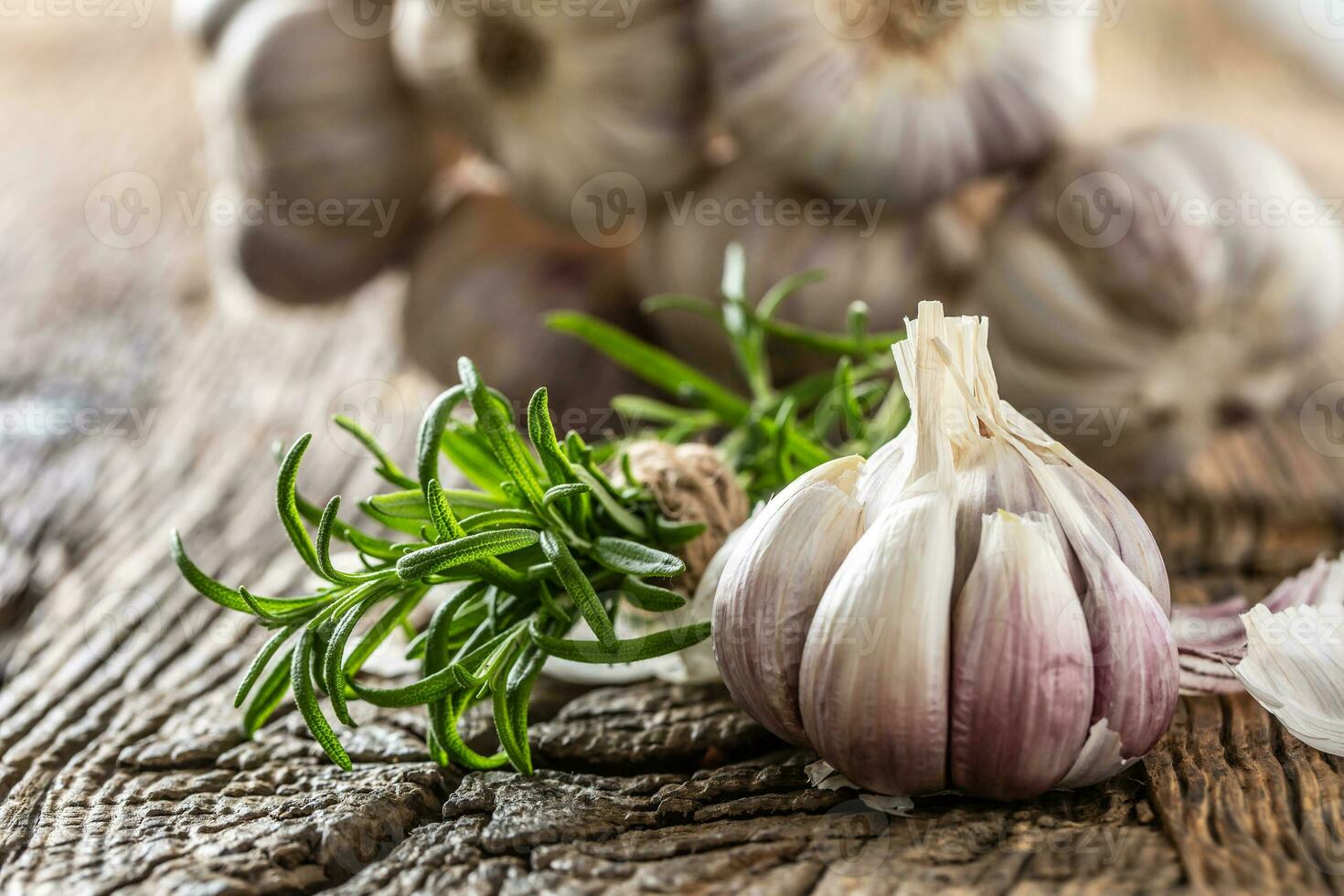 Garlic cloves and bulb with fresh rosemary on old wooden table photo