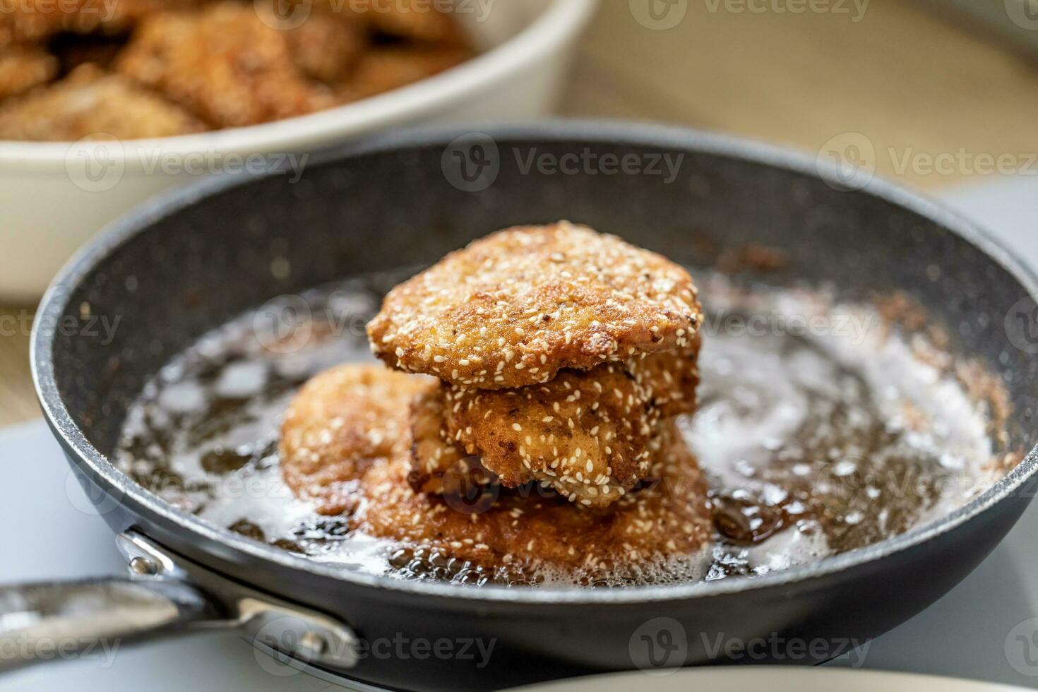 Schnitzels in breadcrumbs piled on a black pan full of frying oil photo