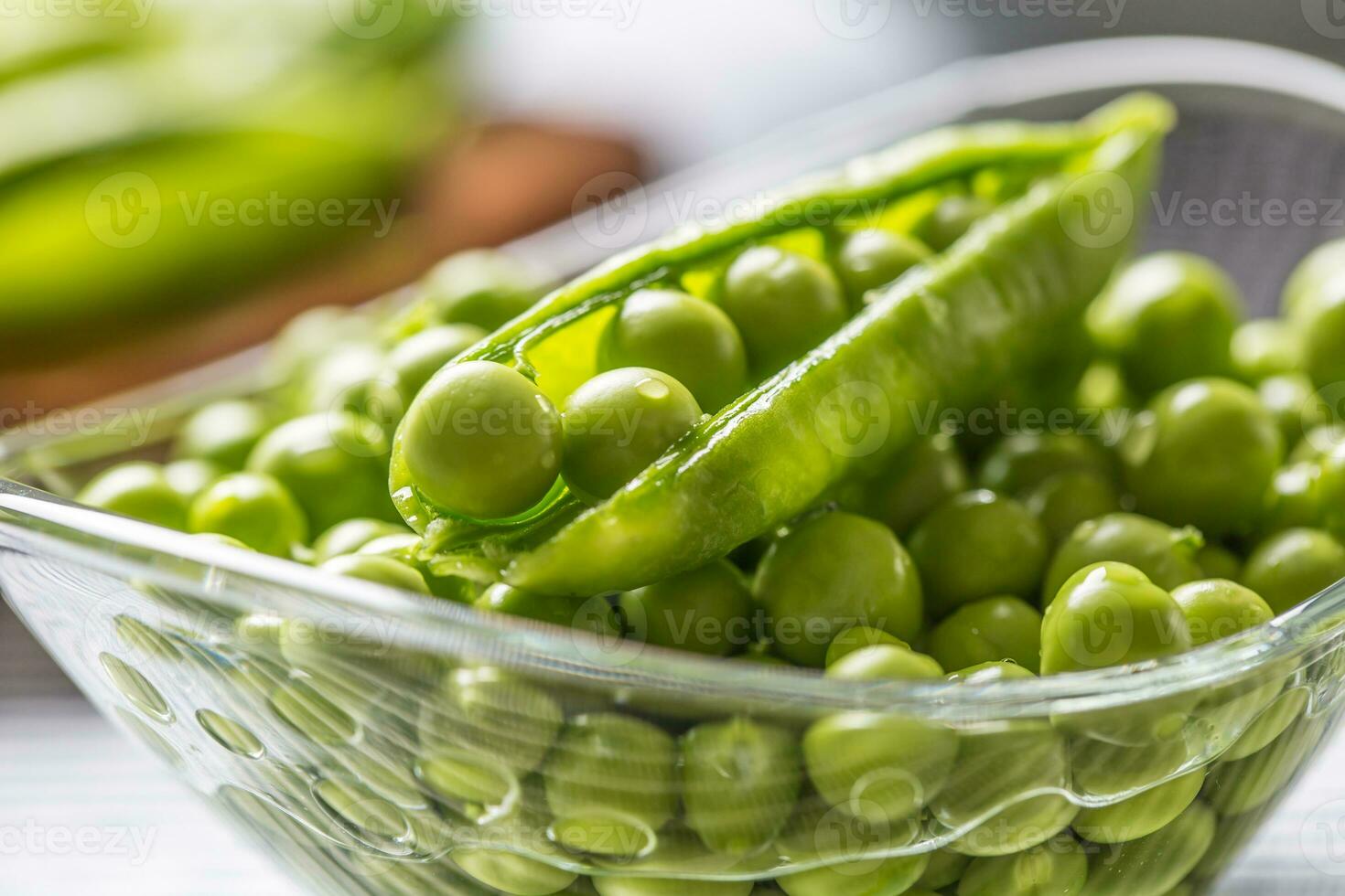 Fresh green pea seeds in bowl on kitchen table photo