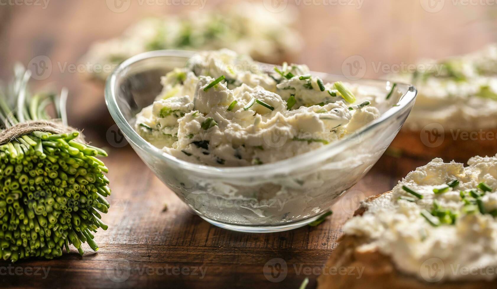 A bowl of homemade cream cheese spread with chopped chives surrounded by bread slices with spread and a bunch of freshly cut chives photo