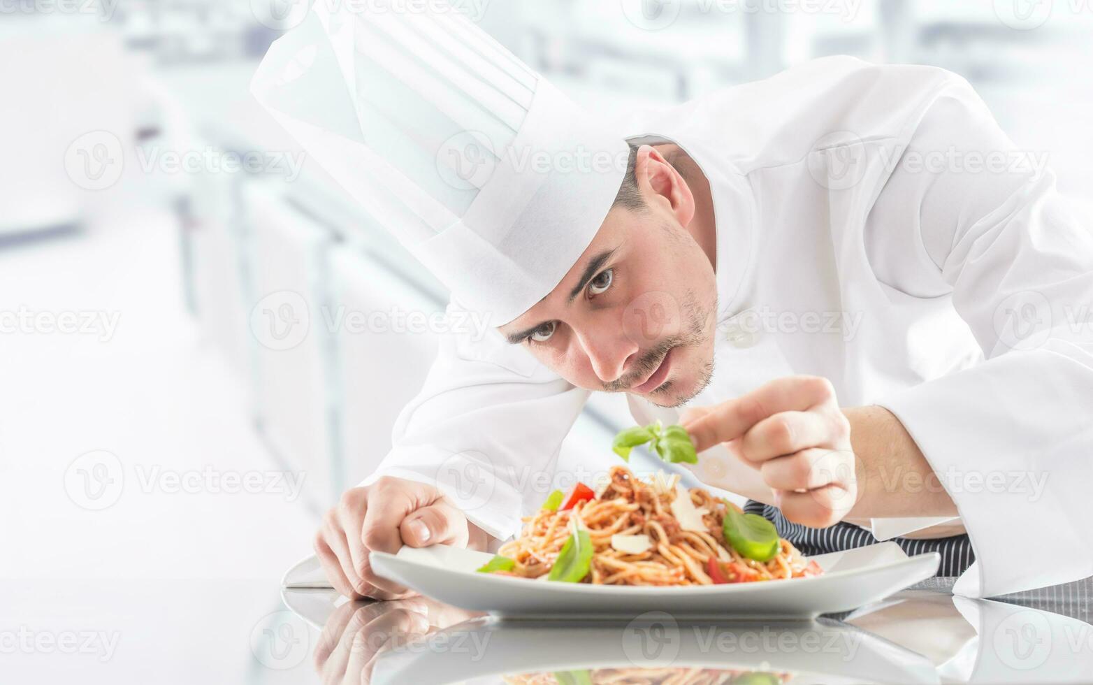 Chef in restaurant kitchen prepares and decorates meal with hands.Cook preparing spaghetti bolognese photo
