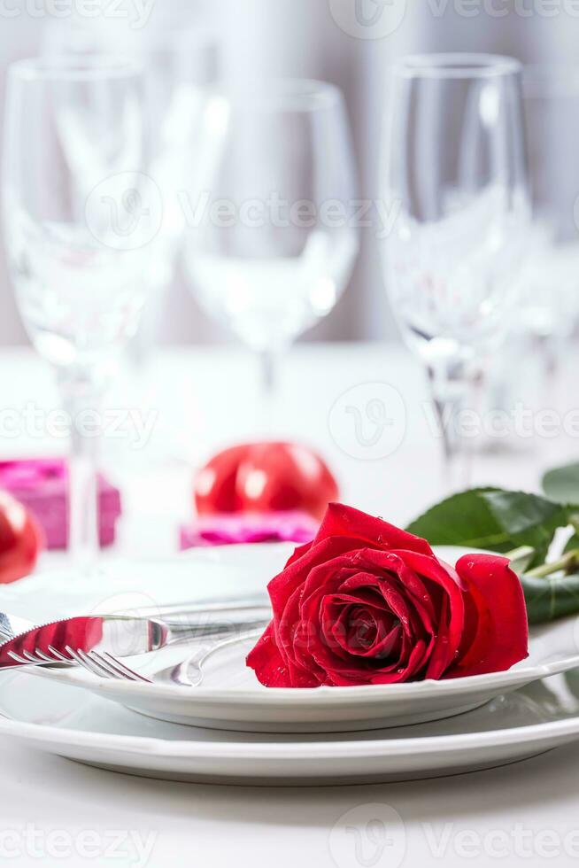 Table setting for valentines or wedding day with red roses. Romantic table setting for two with roses plates cups and cutlery photo