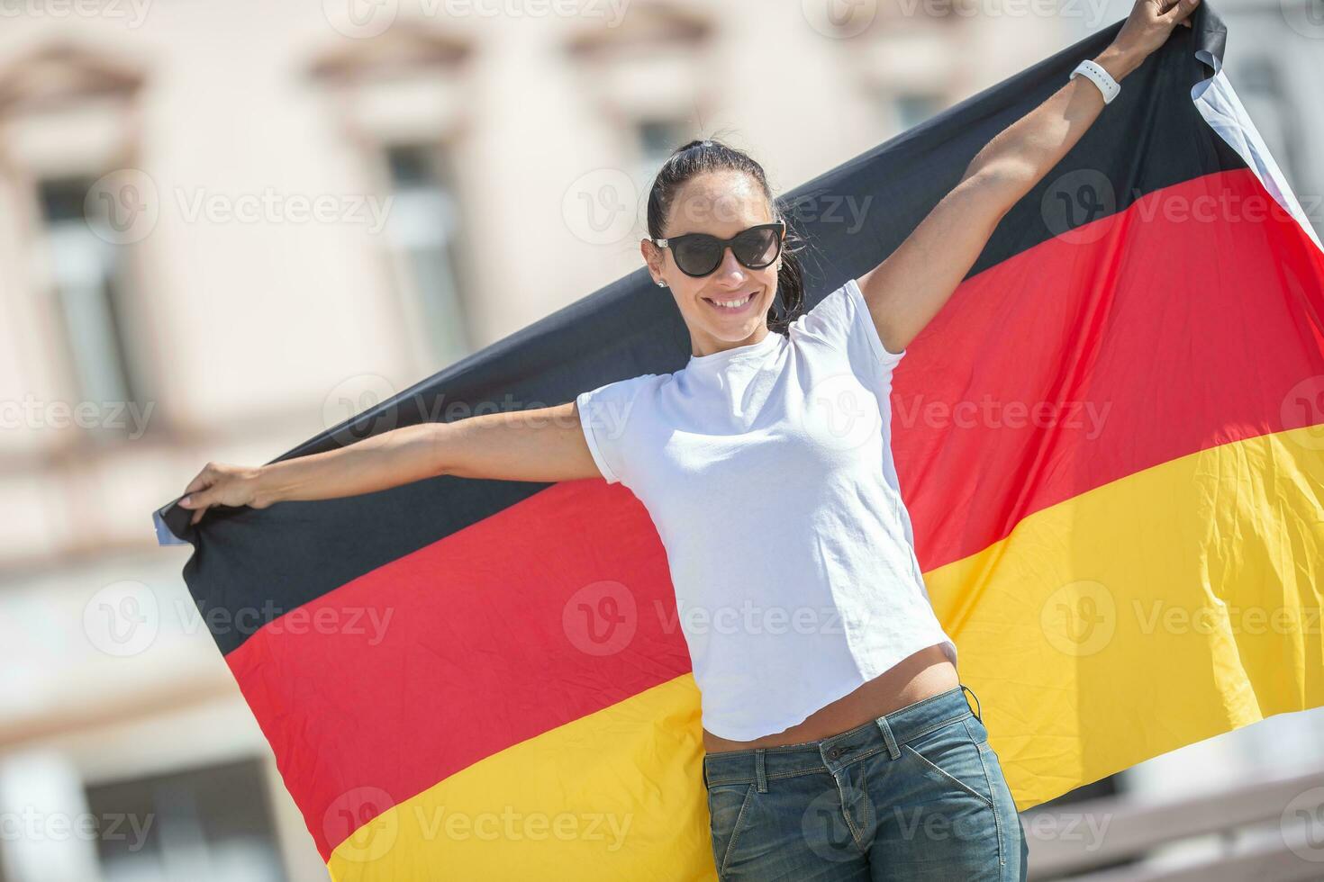 Beautiful smiling girl in sunglasses holds a German flag behind her outdoors photo