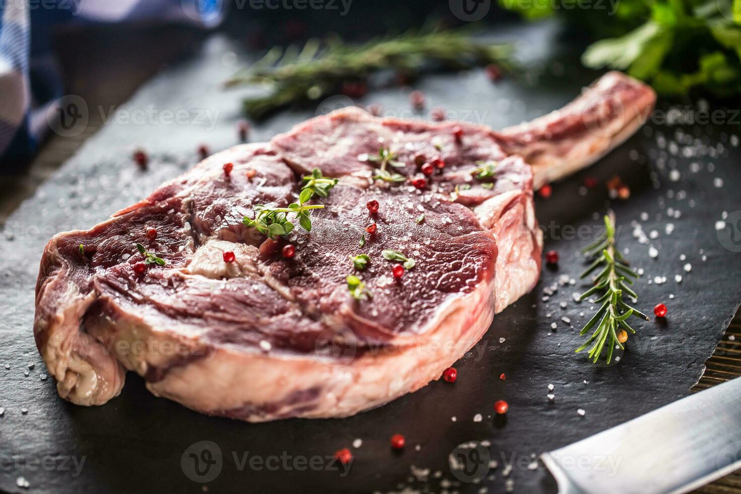Raw beef tomahawk steak with salt pepper and rosemary on slate plate photo