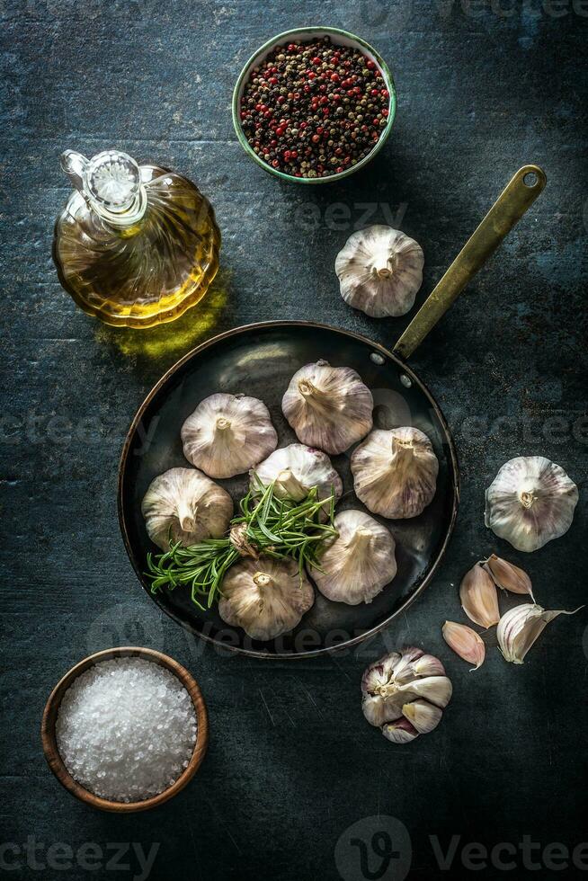Garlic cloves and bulb in pan with fresh rosemary olive oil salt and spice on concrete table photo