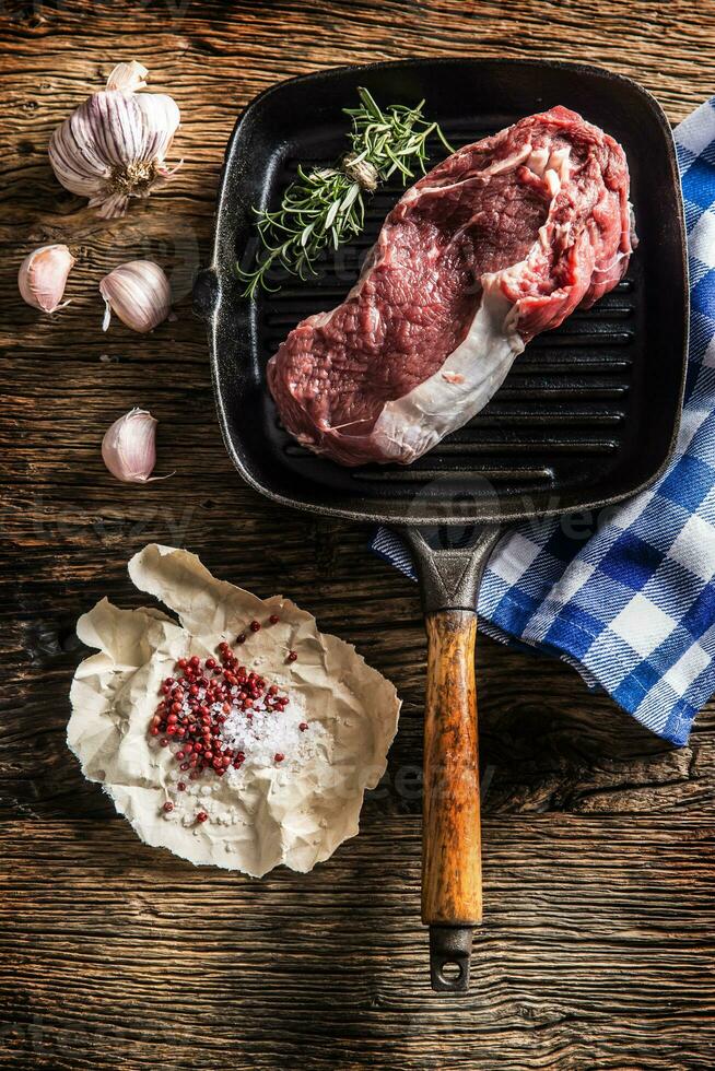 Raw beef steak in grill pan with salt pepper garlic and herbs on wooden table photo