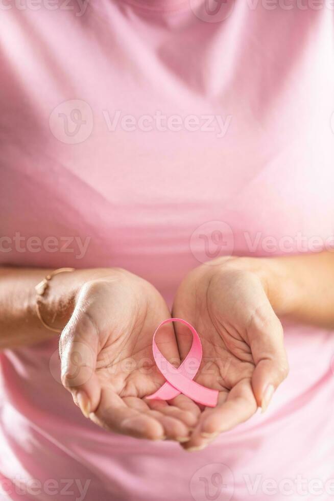 Pink ribbon, an international symbol of breast cancer awareness, is held by a woman in pink shirt photo