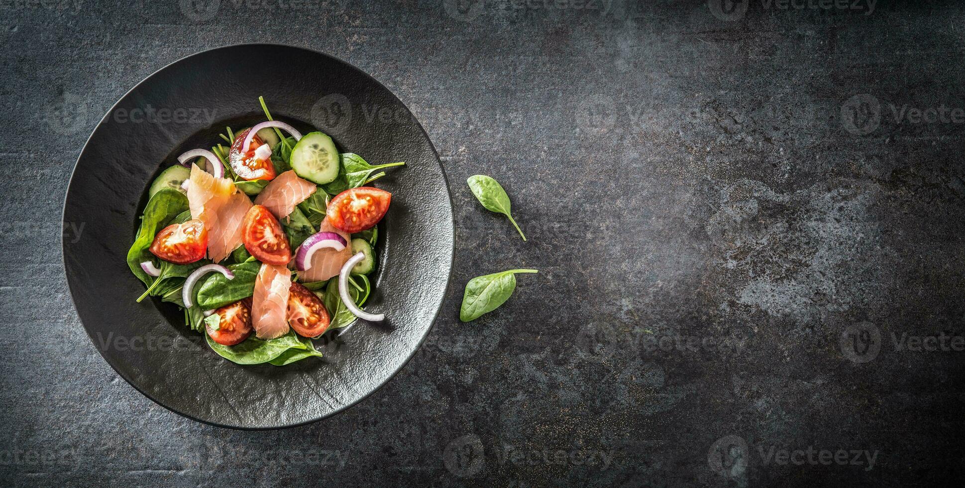 Salmon salad with vegetable in plate on dark kitchen table - Top of view photo