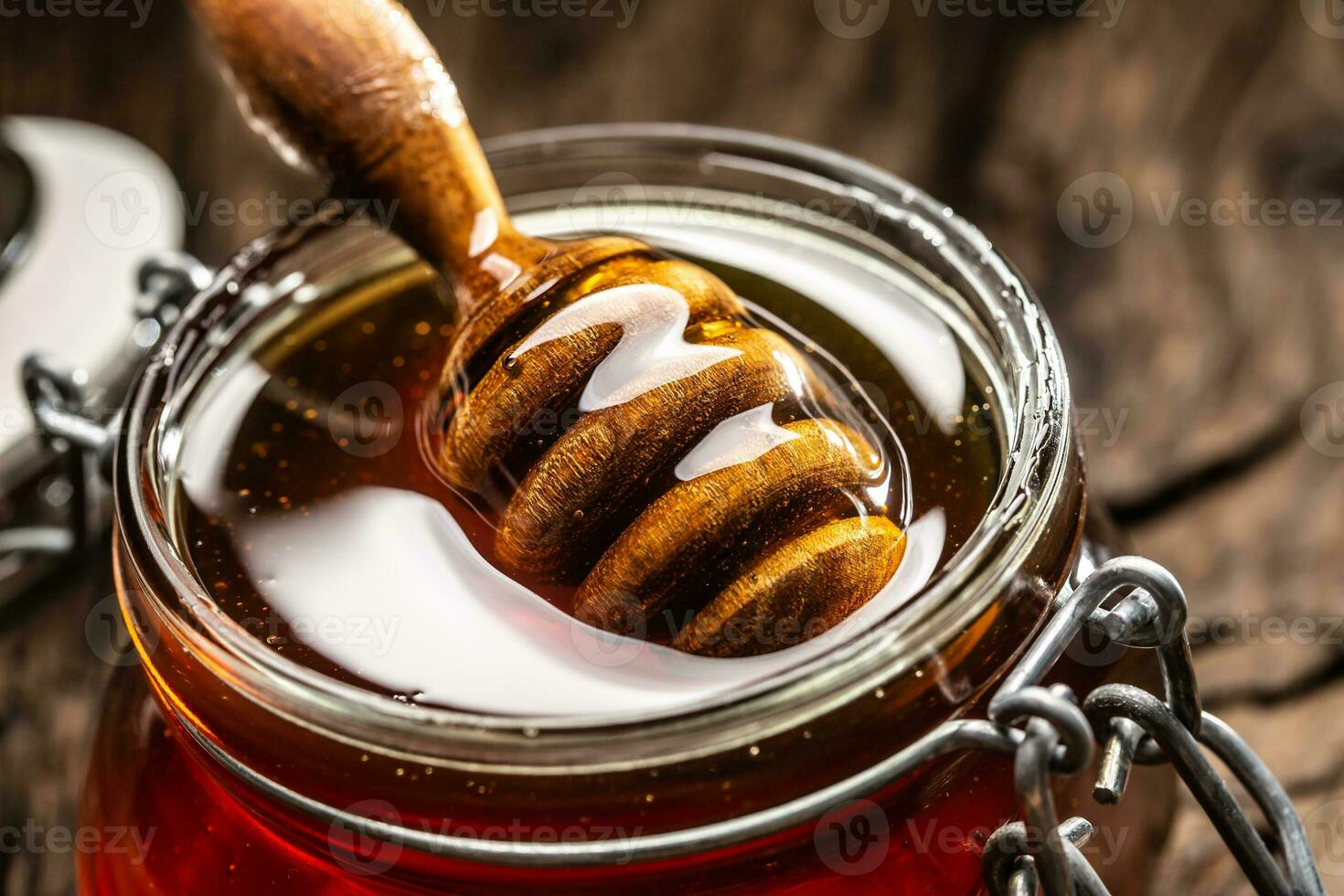 Jar of honey with dipper on wooden table - closeup photo