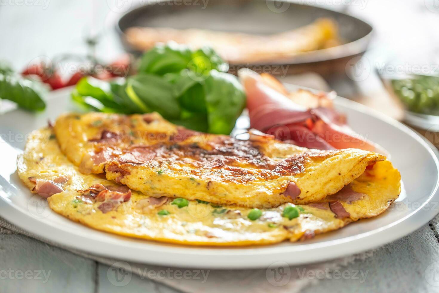 Omelette with prosciutto peas basil tomatoes and herbs on white plate photo