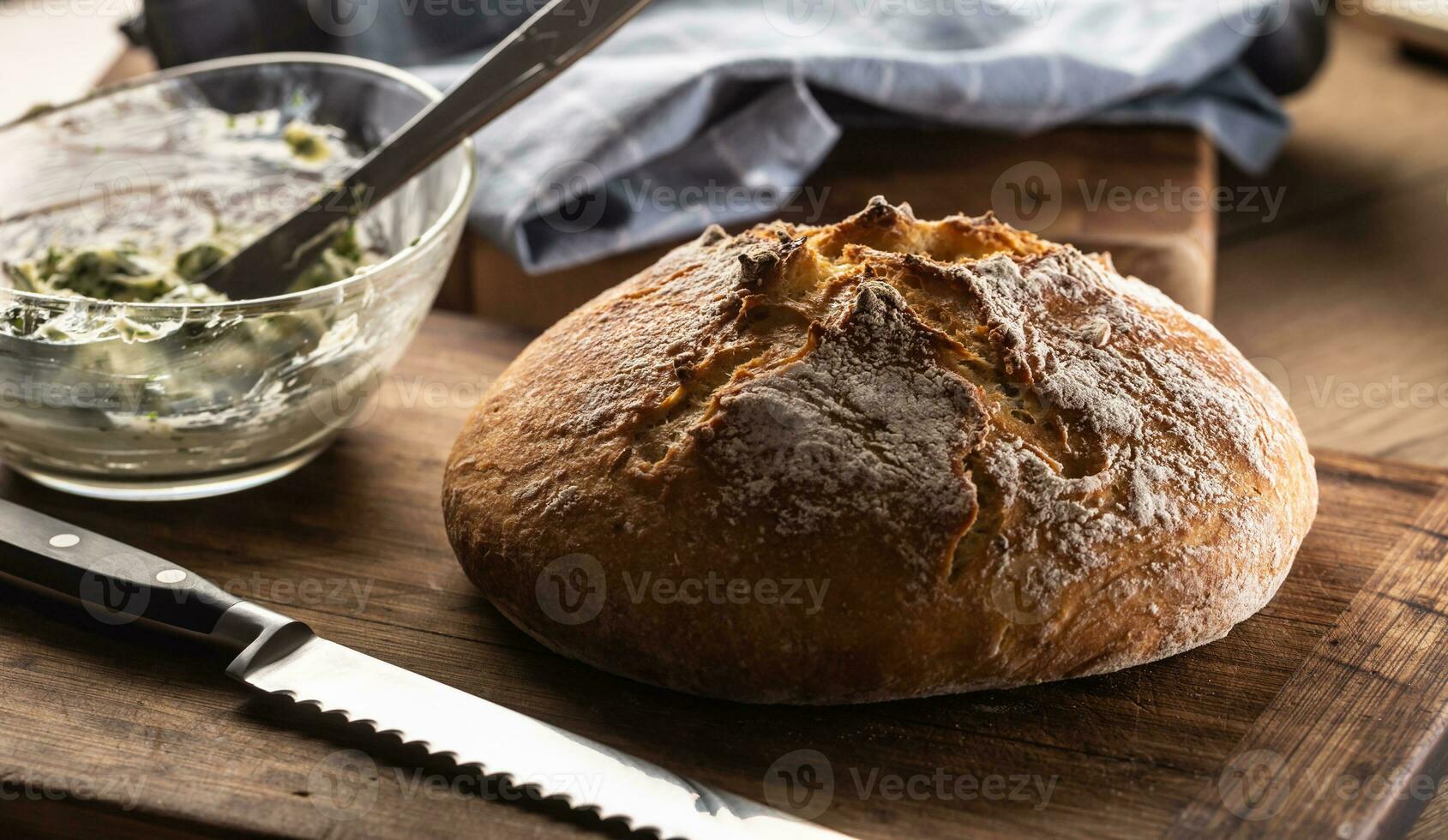 Crusty bread loaf next to a knife and butter mixed with herbs in a bowl photo