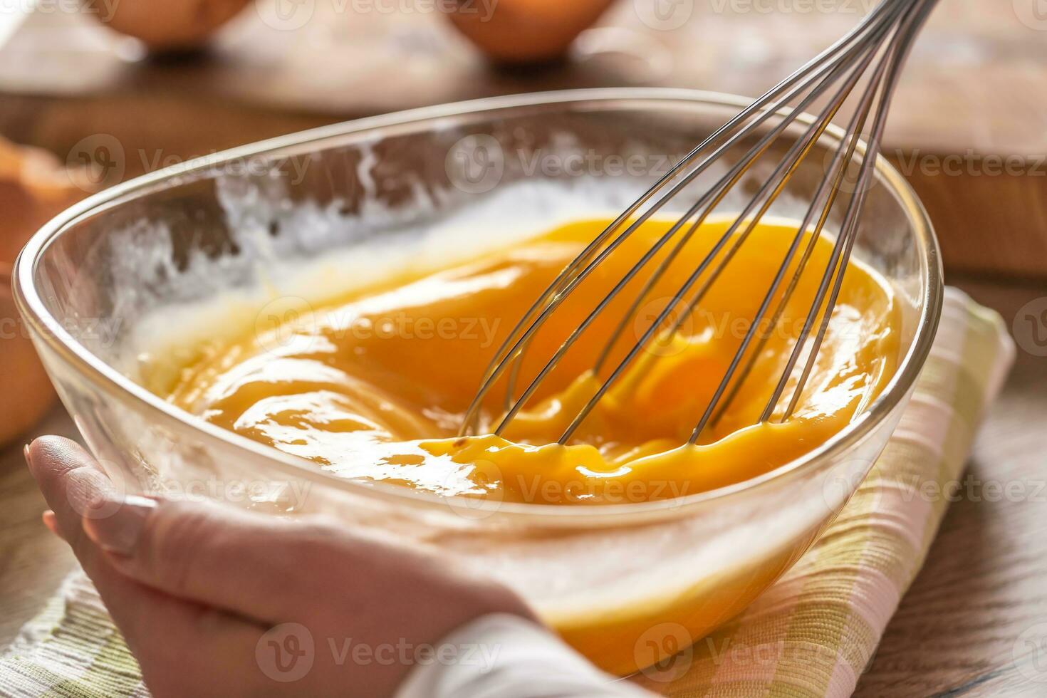 Detail of eggs being whisked in a bowl placed on a towel and wooden table photo